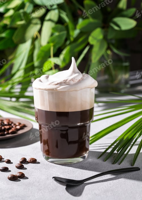 Preview: Iced coffee in a glass with foam on a light background with coffee beans and morning shadows
