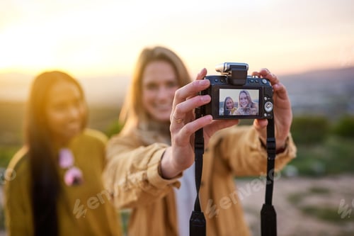 Preview: Shot of two friends taking a selfie with a digital camera while standing outside