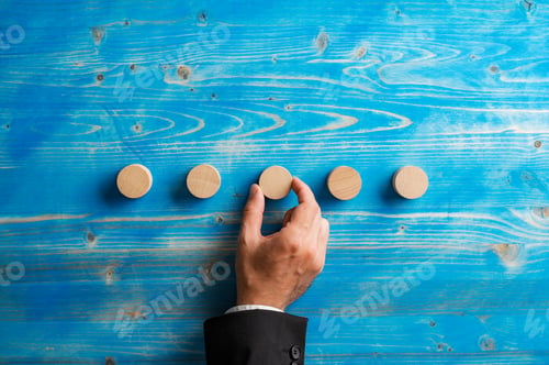 Preview: Businessman placing five simple blank wooden cut circles over blue wooden background