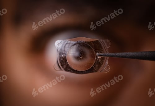 Preview: Close-up of an eye with a contact lens held by tweezers.