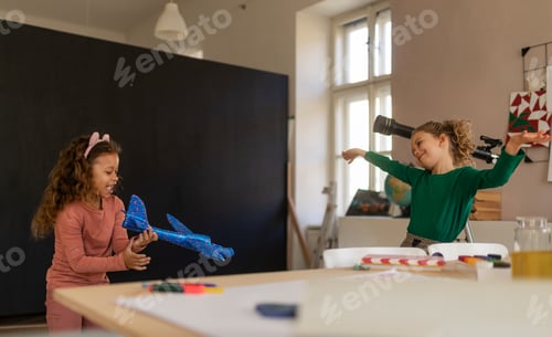 Preview: Happy little girl with her friend having fun together at class indoors at school