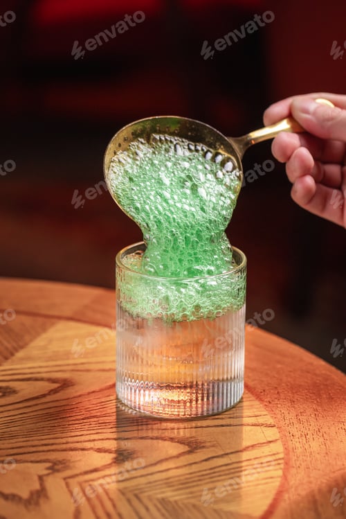 Preview: Green foam cocktail being topped with spoon