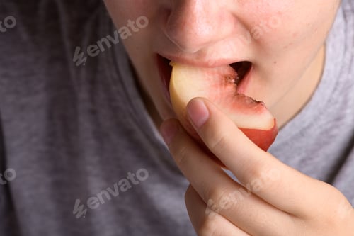 Preview: female hand putting a piece of ripe peach in the mouth, healthy food dessert