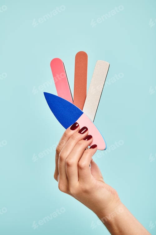 Preview: object photo of different nail files in hand of young unknown lady with nail polish on blue backdrop