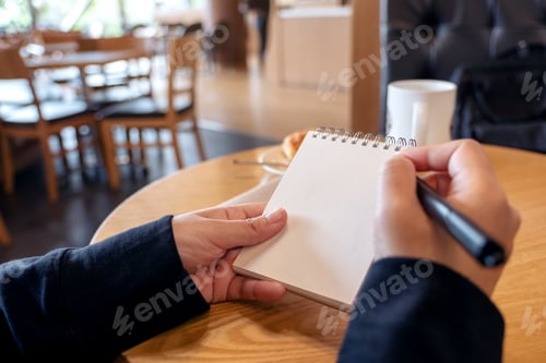 Preview: a woman holding and writing on blank notebook with croissant in a plate on table in cafe