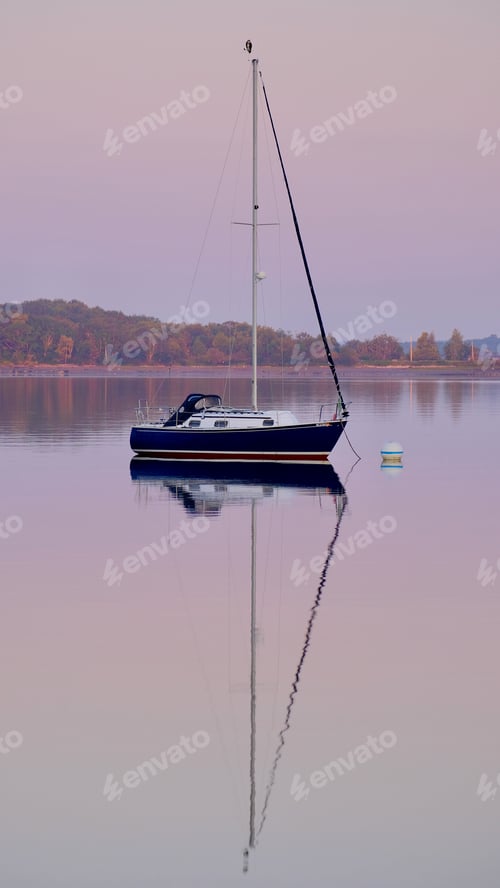 Preview: Vertical shot of a sailboat in the sea with its reflection in the water