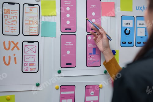 Preview: Web designer pointing at mockups of mobile application screens hanging on whiteboard, planning user