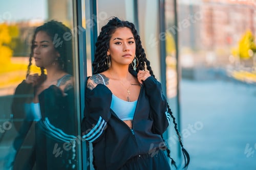 Preview: Urban session. Young woman of black ethnicity with long braids and with tattoos, in some windows