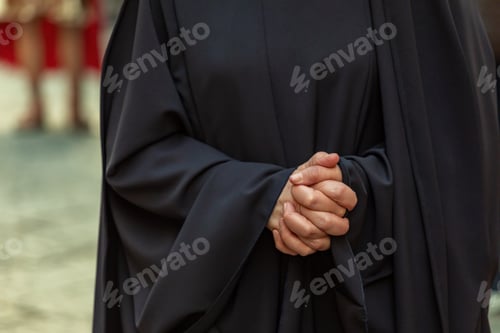 Preview: Close-up of a woman clasping her hands in prayer, wearing a black cassock during procession.