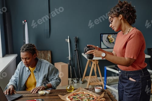 Preview: Young Black Woman Photographing Pizza While Black Man Working