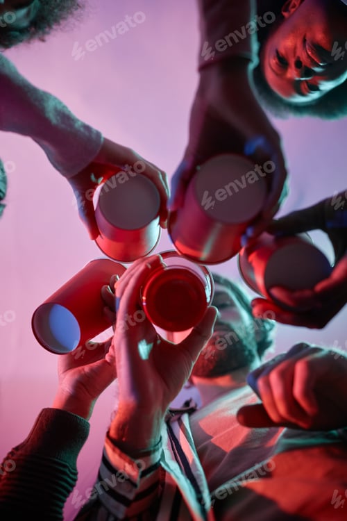 Preview: Group of young people clinking red cups with alcohol in pink neon light