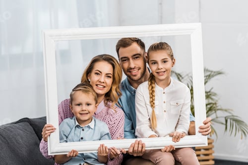 Preview: happy family holding white frame and looking at camera in living room