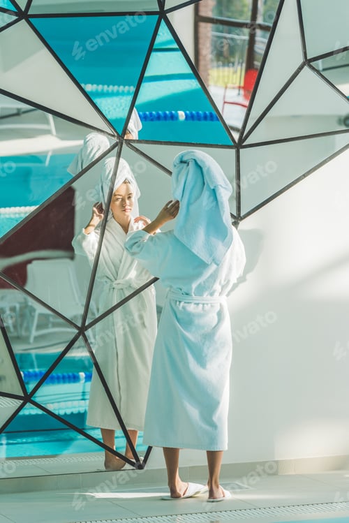 Preview: young woman in bathrobe and towel looking at mirror in spa center