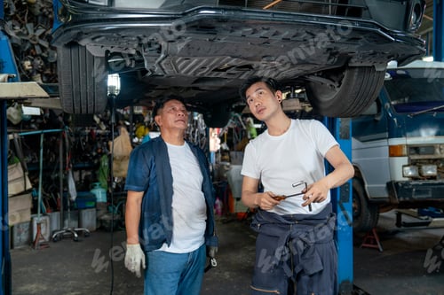 Preview: Senior mechanic and young man help to fix the problem of car in area under the car in garage.