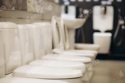 Preview: Exhibition of samples of white toilet bowls standing in a row in the warehouse of a plumbing store