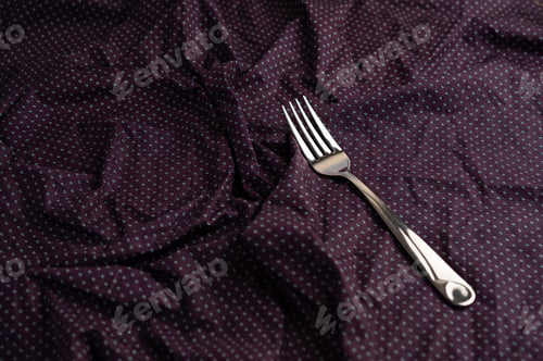 Preview: The fork is placed on a purple wrinkled fabric.