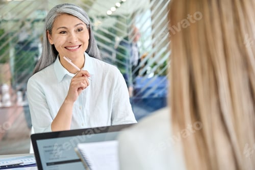 Preview: Older mature Asian manager talking to younger colleague intern trainee.