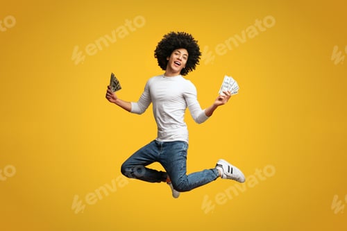 Preview: Excited young man jumping with money on orange background