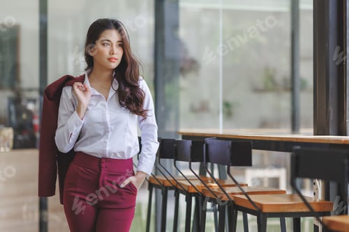 Preview: Young businesswoman standing in modern office, thinking