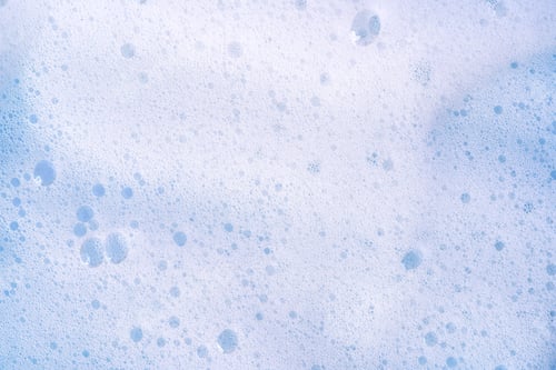 Preview: Texture of white foam on blue backdrop. Foam cosmetic product for selfcare procedure.