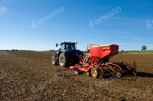 Preview: Rear view of farmer driving tractor with seed drill in ploughed field in spring