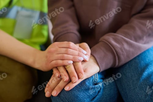 Preview: Hand of female volunteer in uniform covering that of young refugee