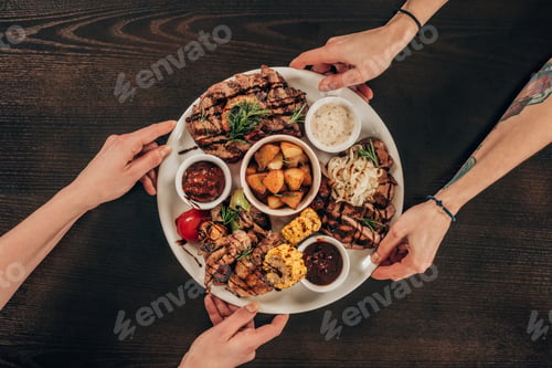 Preview: cropped image of lesbian couple holding plate with beef steaks, chicken wings and grilled vegetables