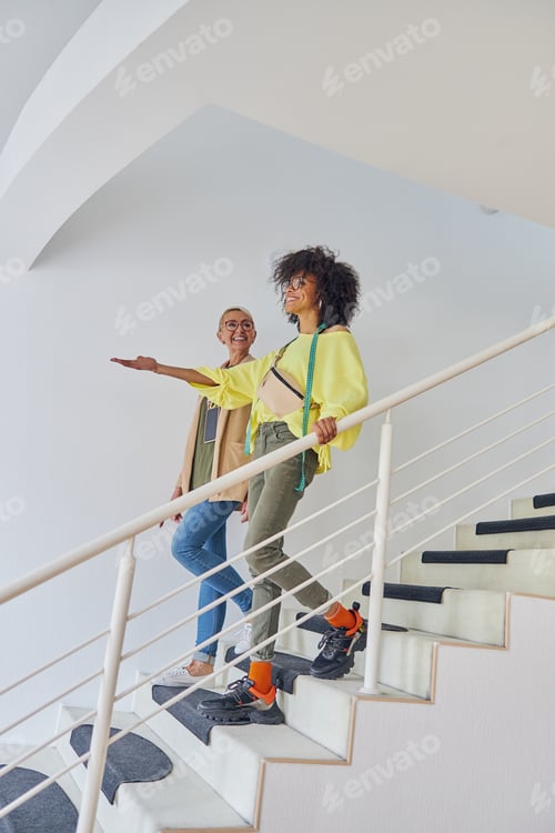 Aperçu: African-American dressmaker points on something in front to mature colleague going down on steps