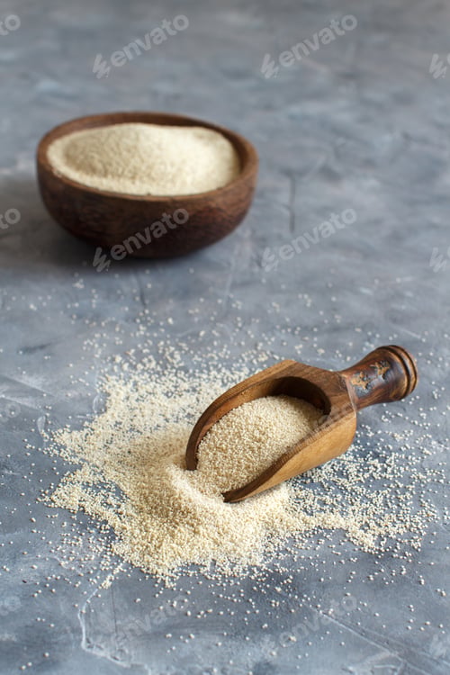Preview: Raw uncooked fonio seeds with a spoon in a bowl on grey background