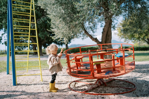Preview: Little girl stands near the carousel on the playground