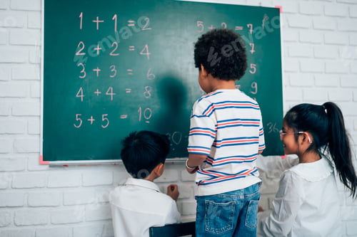 Preview: little child standing at chalkboard and writing math formula on blackboard.