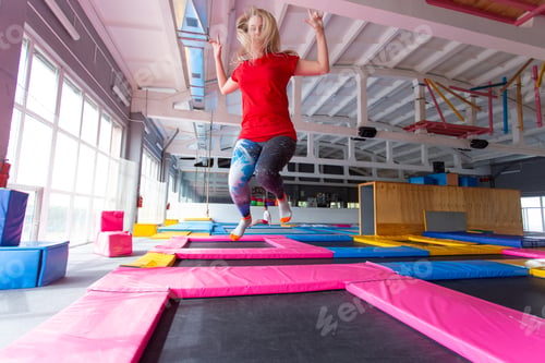 Preview: Fitness, fun, leisure and sport activity concept - Young happy woman jumping on a trampoline indoors