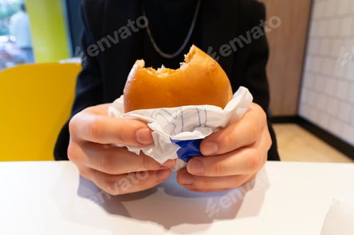 Preview: Hands holding a veggie burger in an unfolded paper with a bitten edge close-up, selective focus.Hand