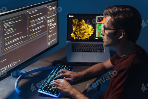 Preview: Closeup of program developer writing software on multiple computer screens at home office