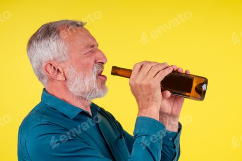 Preview: senior man drinking alcohol alone studio yellow baclground