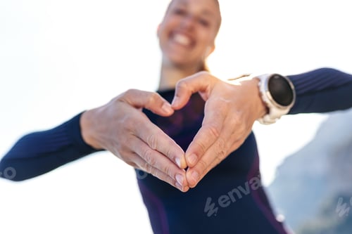 Preview: Sporty young woman making heart shape with hands while posing to