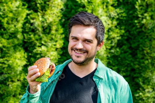 Preview: Casual man in green shirt with burger in outdoors