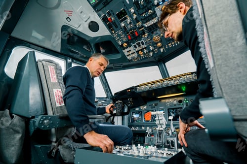 Preview: An experienced pilot instructs a young student before a training flight in the cockpit simulator