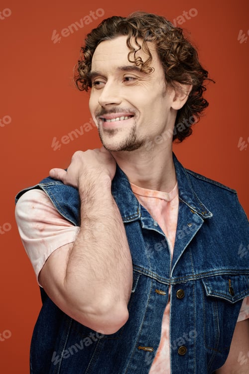 Preview: Handsome Man With Curly Hair Smiling Against a Vibrant Orange Backdrop
