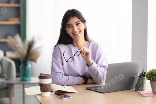 Preview: Cheerful millennial lady sitting at desk and posing with glasses