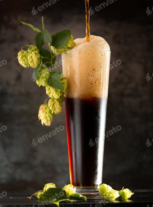 Preview: Glass of dark beer with hops around on a dark background