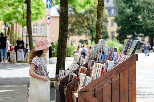 Preview: A teenage girl choosing books near a street bookstand on a summer day