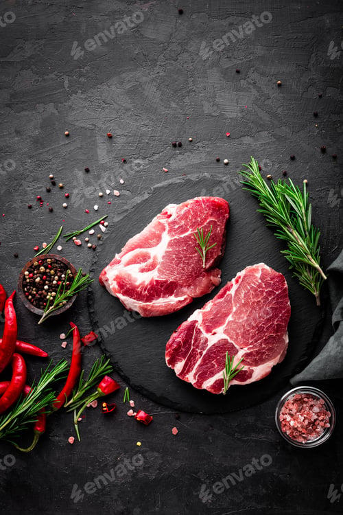 Preview: Raw pork meat. Fresh steaks on slate board on black background. Top view