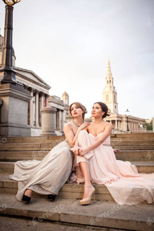 Preview: Two women in elegant dresses posing on city steps at dusk