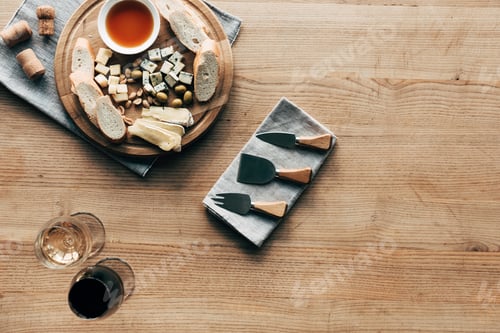Preview: top view of wine glasses, sauce, bread, cheese, olives, corks and cooking utensils on wooden surface