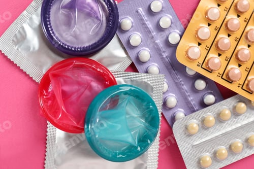 Preview: Blisters of contraceptive pills and condoms on pink background, flat lay