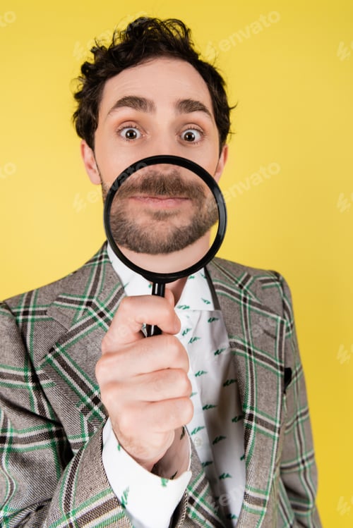 Preview: Wide angle view of stylish man in jacket holding magnifying glass isolated on yellow