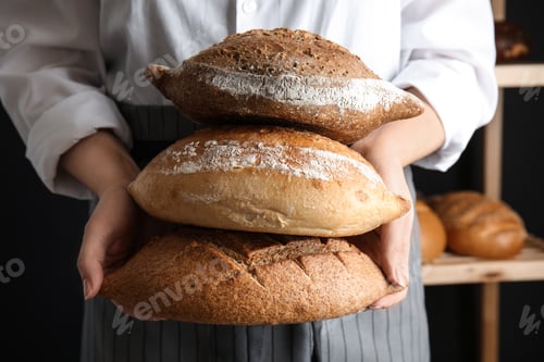 Preview: Baker holding loaves of bread indoors, closeup
