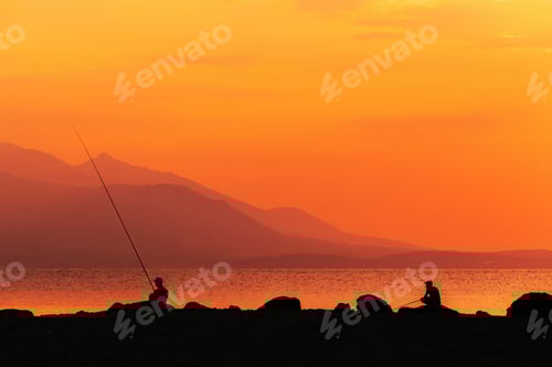 Preview: Fishing at the Aegean sea coast in summer sunrise, silhouette of fisherman with rod at the coastline