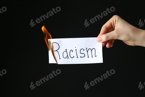 Preview: Woman holding burning card with word Racism on black background, closeup